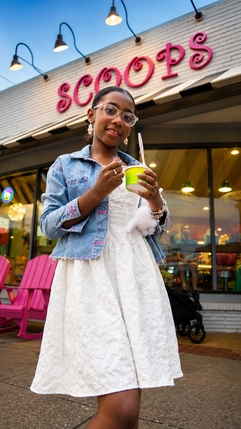 Young girl photographed outside a colorful ice cream shop at dusk